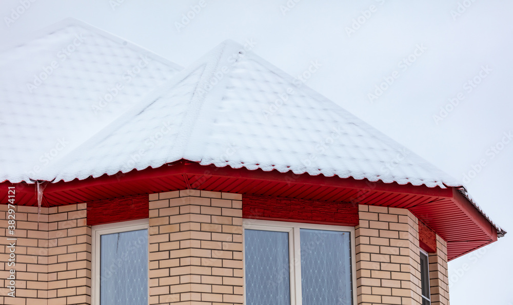 Naklejka premium White snow lies on the red roof of the house.