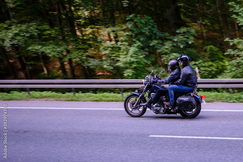 Motorbike riding on the road with barriers and forest in the background.