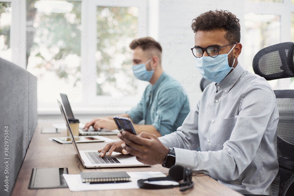 Young creative coworkers working with new startup project in modern business office. Group of young busnessmen working wearing medical protective masks. Teamwork, self care, business lifestyle concept Young creative coworkers working with new startup project in modern business office. Group of young busnessmen working wearing medical protective masks. Teamwork, self care, business lifestyle concept