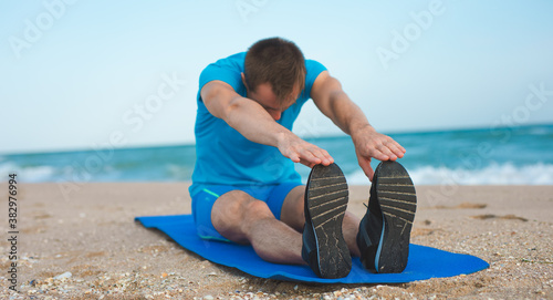 Man stretching on a yoga mat at the beach