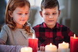 Small girl and boy indoors at home at Christmas, holding candles.