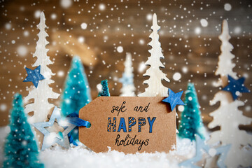 Label With Engllish Text Safe And Happy Christmas. White And Green Christmas Tree With Stars. Snow, Snowflakes And Wooden Background