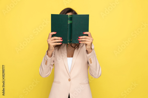 young businesswoman in pink suit hiding behind book