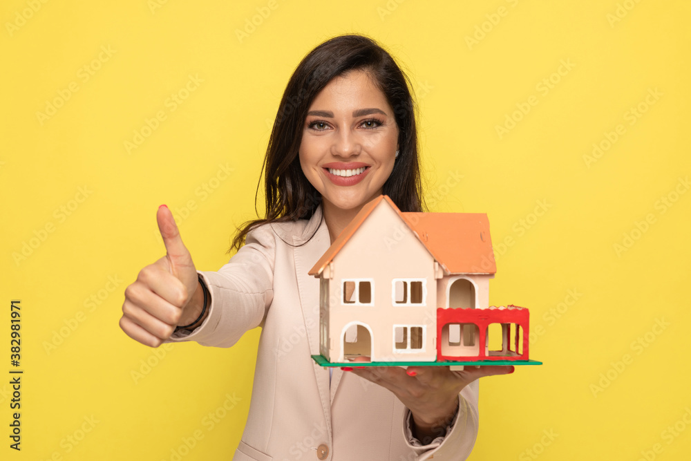 young woman making thumbs up gesture and showing building model young woman making thumbs up gesture and showing building model
