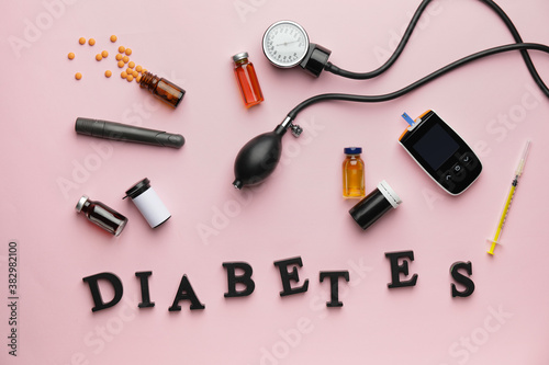 Glucometer with medications, sphygmomanometer and word DIABETES on color background