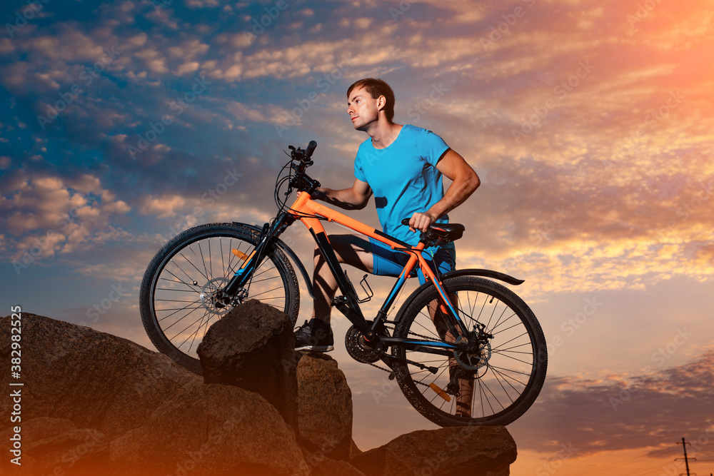 Fototapeta premium Young man with bicycle against cloudy sky background