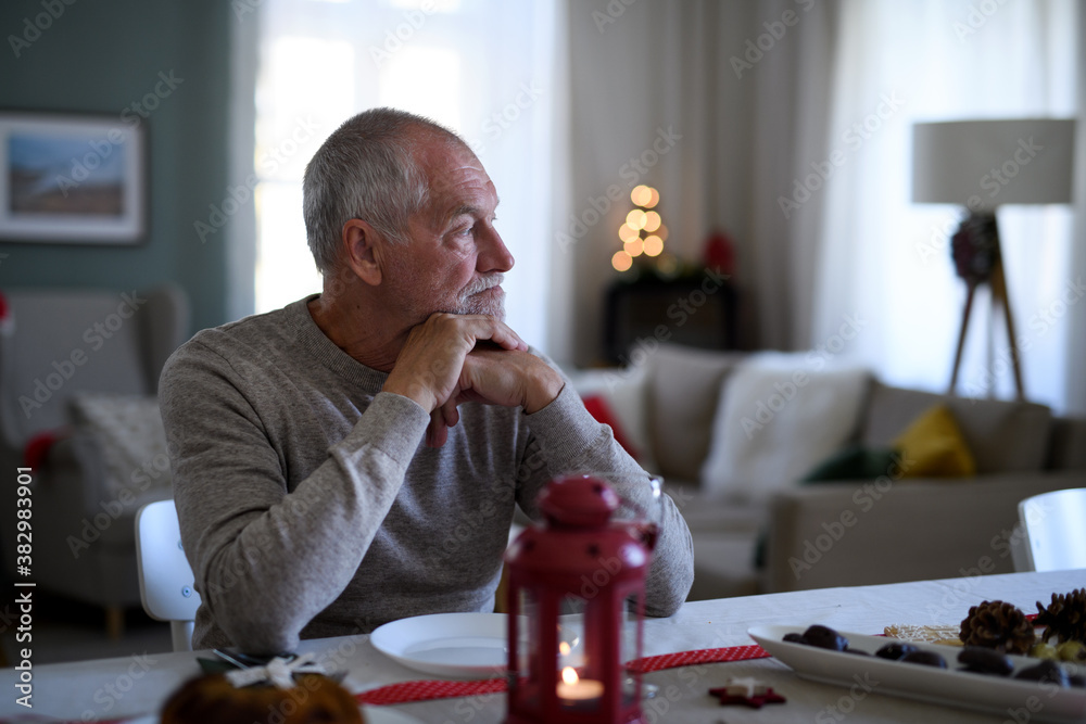 Lonely senior man sitting at the table indoors at Christmas, solitude concept. - obrazy, fototapety, plakaty 