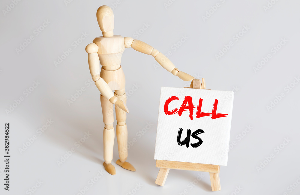 Wooden man shows with a hand to white easel with text CALL US on white background Wooden man shows with a hand to white easel with text CALL US on white background