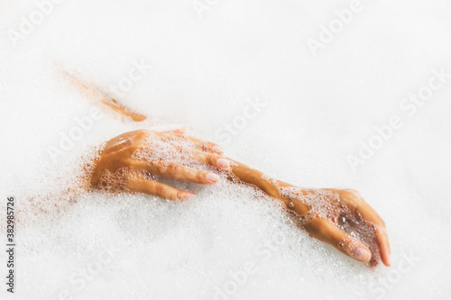 Woman hands in bath full of foam bubbles close-up. Spa beauty treatment. photo