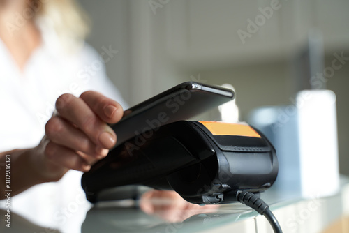 Woman using her smartphone near credit card reader