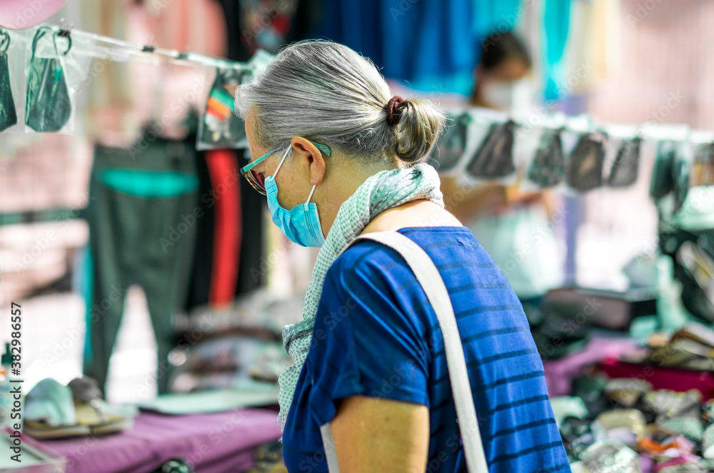 A white haired senior woman wearing a medical mask due to coronavirus while shopping at the market.