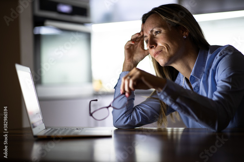 Pretty, middle-aged woman working late in the day on a laptop computer at home, running a business from home/working remotely for a corporation photo