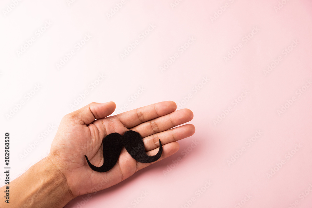 The man uses hand holding black mustache, studio shot isolated on white background, Prostate cancer awareness month, Fathers day, minimal November moustache concept The man uses hand holding black mustache, studio shot isolated on white background, Prostate cancer awareness month, Fathers day, minimal November moustache concept