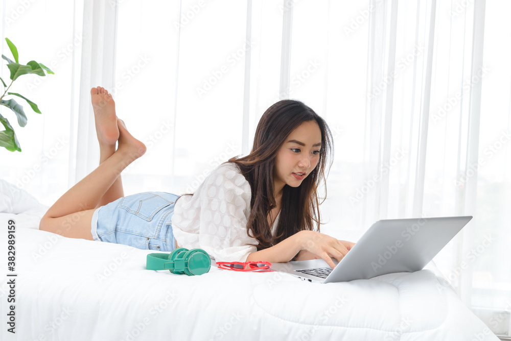 Beautiful young Asian woman relaxing and using a lapto on her bed. Beautiful young Asian woman relaxing and using a lapto on her bed.