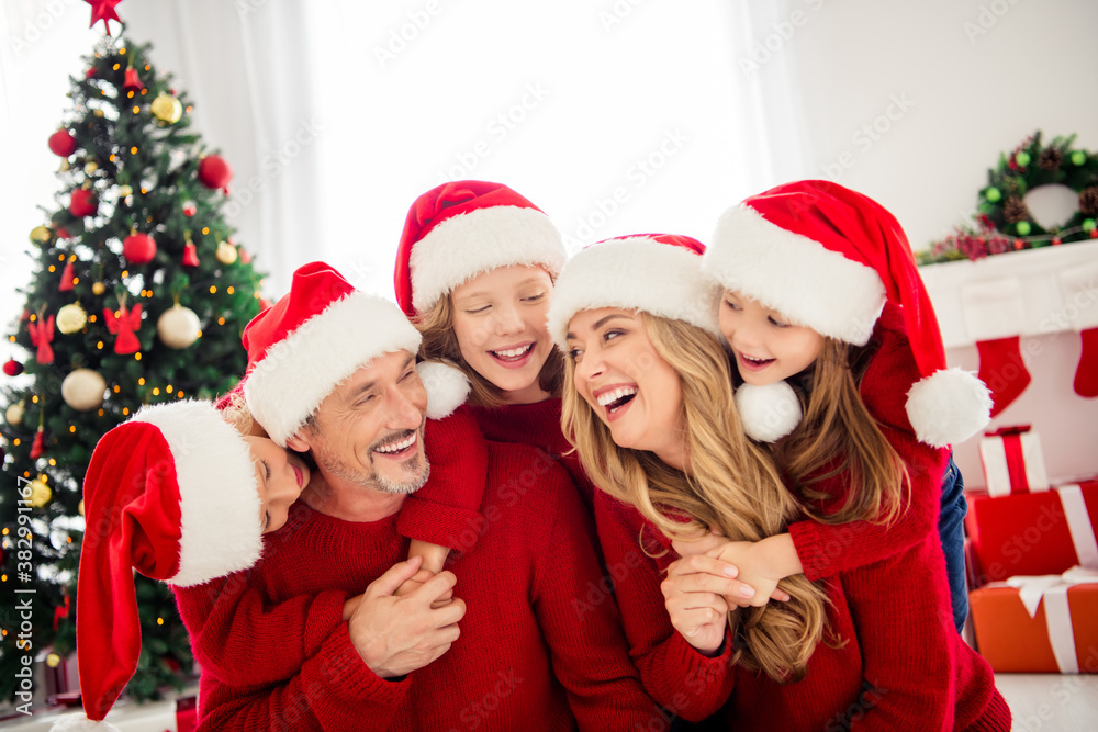Full family x-mas christmas advent gathering. Little preteen kids hug embrace mommy daddy dad mom wear santa claus cap in house indoors with eve noel ornament decoration Full family x-mas christmas advent gathering. Little preteen kids hug embrace mommy daddy dad mom wear santa claus cap in house indoors with eve noel ornament decoration