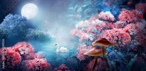 Fototapeta Naklejka Na Ścianę i Meble -  Fantasy Magical Enchanted Fairy Tale Landscape With Swan Swimming In Lake, Fabulous Fairytale Blooming Pink Rose Flower Garden And Mushrooms On Mysterious Blue Background And Glowing Moon Ray In Night