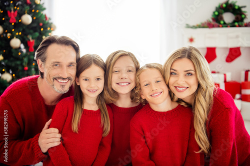 Photo of full family five people meeting three little kids cuddle toothy beaming shiny smiling wear red jumper in living room decorated x-mas tree lights gift boxes indoors