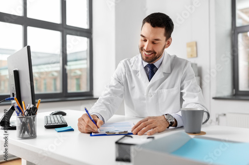 healthcare, medicine and people concept - smiling male doctor with clipboard at hospital