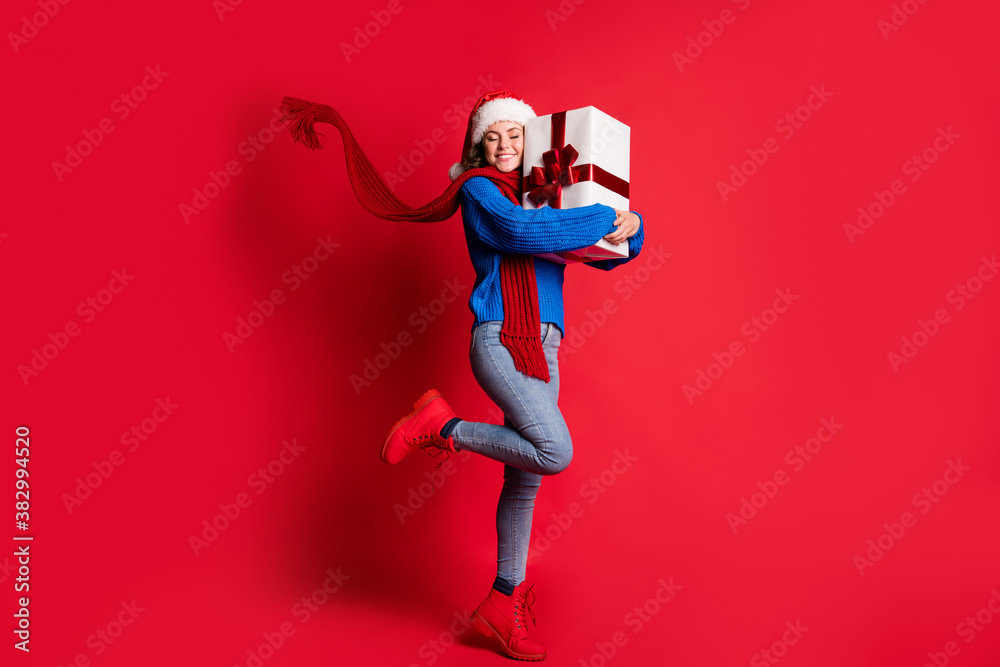 Photo portrait full body cheerful woman hugging present box smiling closed eyes standing on one leg scarf flowing isolated on bright red colored background