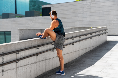 fitness, sport, training and lifestyle concept - young man in headphones stretching leg outdoors © Syda Productions