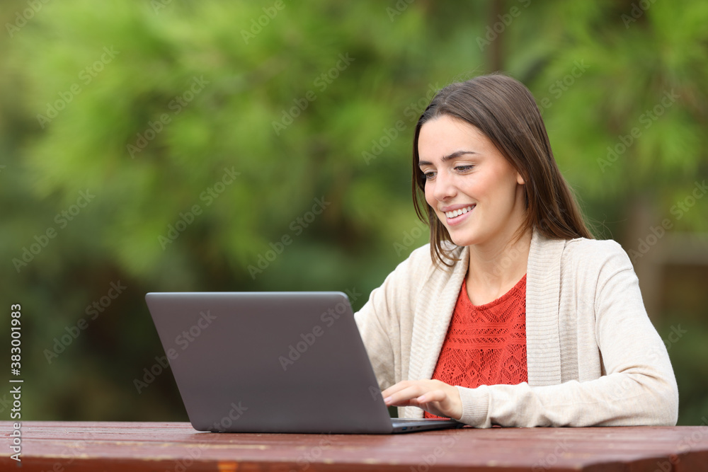 Happy woman using laptop sitting in a park table Happy woman using laptop sitting in a park table