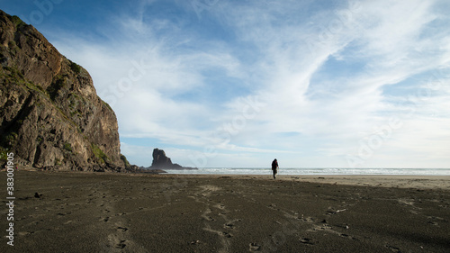 Walking on the black-sand Anawhata beach with keyhole rock in the distance, Waitakere, Auckland