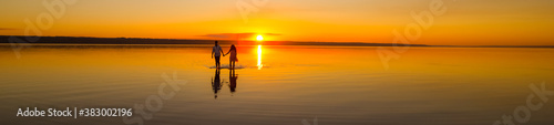 Young couple is walking away in the water on summer beach. Sunset over the sea.Two silhouettes against the sun. Just married couple in romantic love story. Man and woman in holiday honeymoon trip.