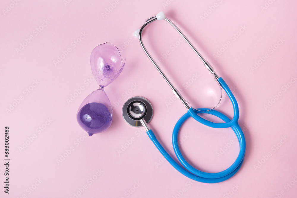 Fototapeta premium stethoscope and broken hourglass on pink background