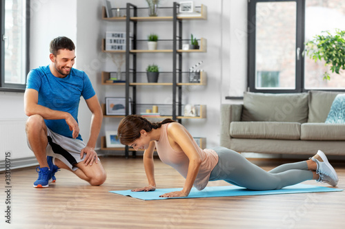 fitness, sport, training and lifestyle concept - happy smiling woman with personal trainer doing push-ups at home