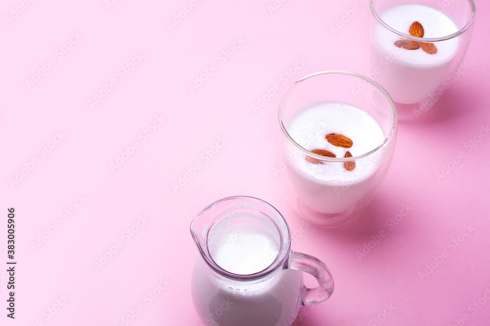 Almond milk in a decanter and two glasses on a pink background. Empty space for text