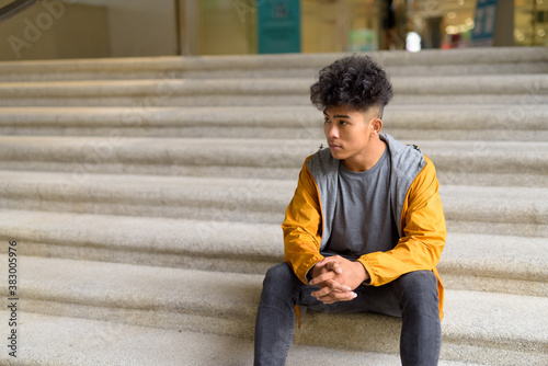 Young Asian man with curly hair sitting on staircase in the city