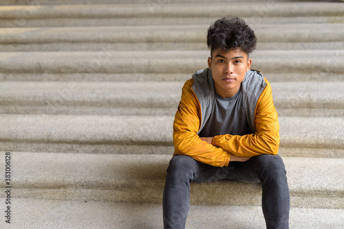 Young Asian man sitting with arms crossed on staircase in the city