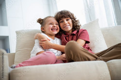 Girl with brother is hugging on sofa