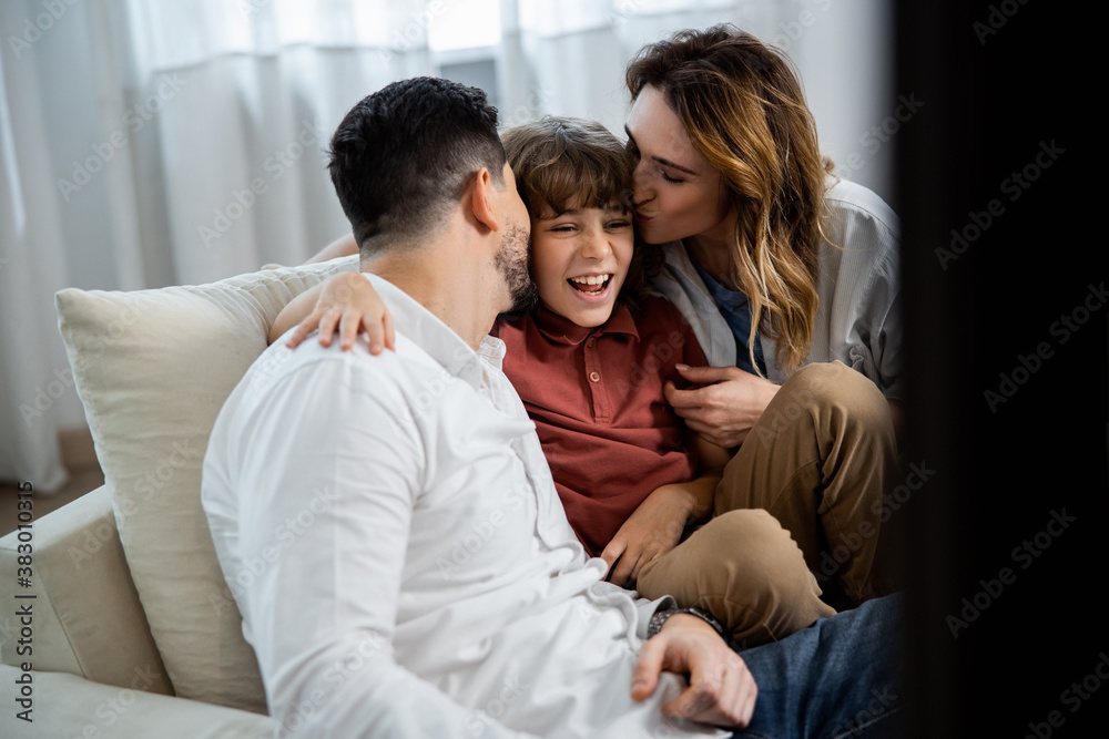 Boy sitting between his parents and hugging them Boy sitting between his parents and hugging them