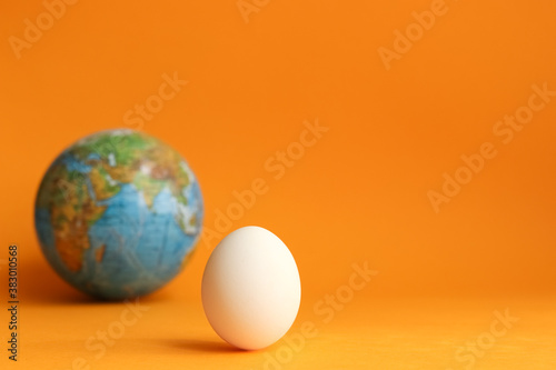 White hen's egg and blue earth globe on orange background for world egg day partial focus