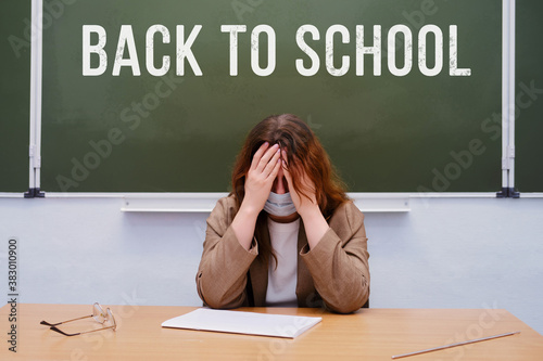 Crying teacher sits in a school class with the text "Back to school"