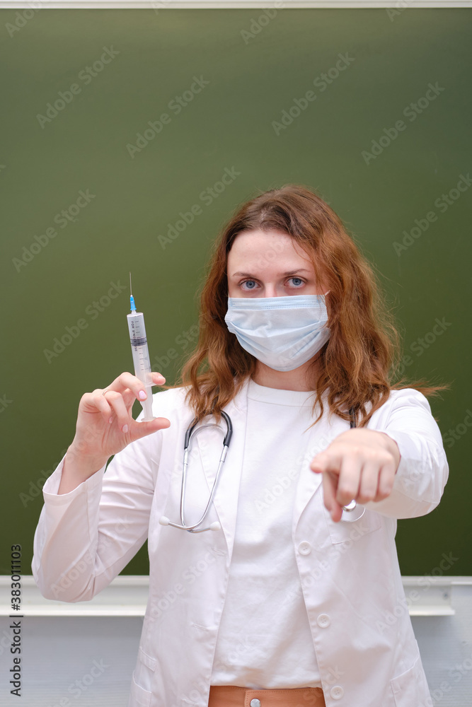 Doctor with a big syringe in a school class points a finger at you. School education during the coronavirus epidemic Doctor with a big syringe in a school class points a finger at you. School education during the coronavirus epidemic