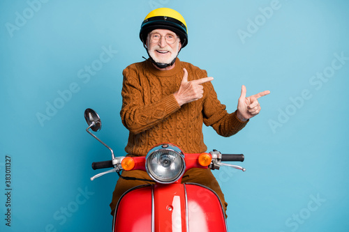 Portrait of his he nice attractive cheerful cheery glad bearded grey-haired man riding moped showing copy space advice recommend idea solution isolated over blue pastel color background photo