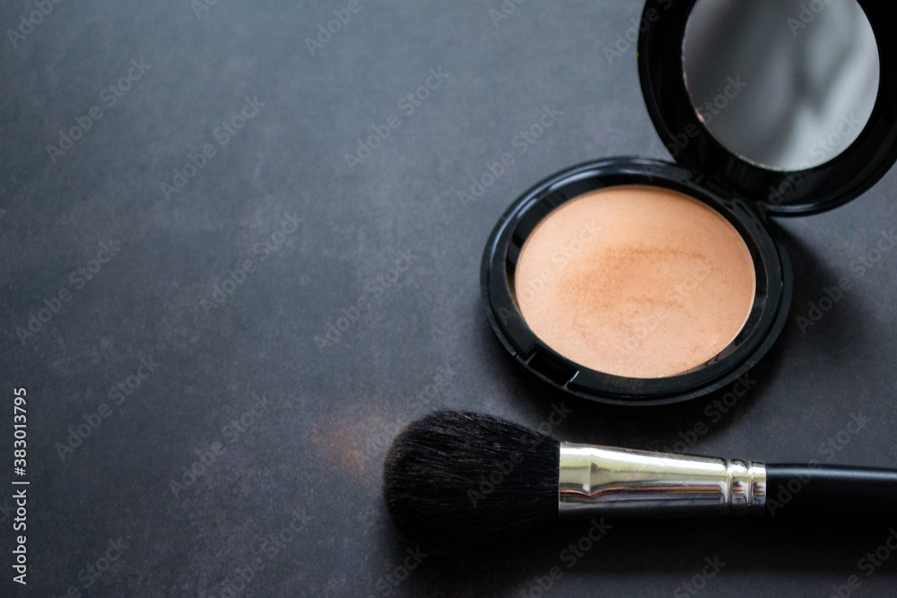 Top view of a black makeup brush and an open box of pink powder with mirror. Black background. Copy space Top view of a black makeup brush and an open box of pink powder with mirror. Black background. Copy space