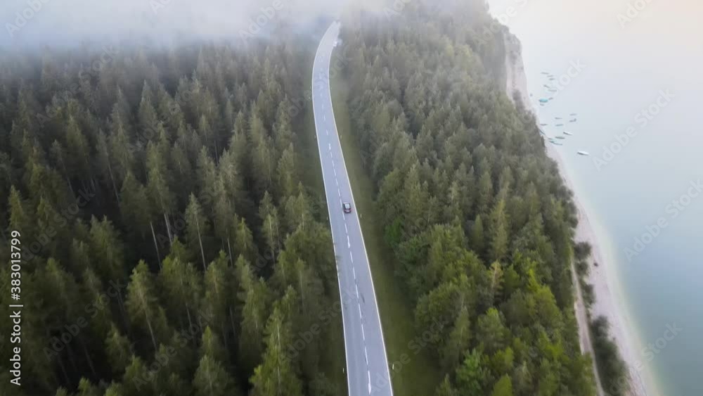 Aerial shot flying through a cloud of a car driving on a mountain road surrounded by nature