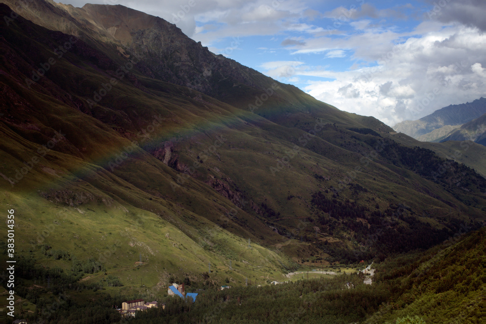 Rainbow over a green valley surrounded by mountains. Caucasus, Russia.