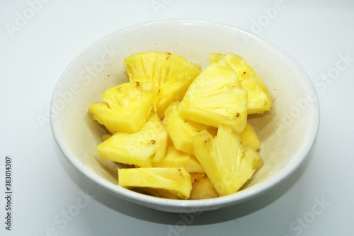 A white bowl containing fresh, ripe pineapple pieces with a white background