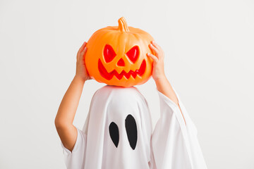 Funny Halloween Kid Concept, little cute child with white dressed costume halloween ghost scary he holding orange pumpkin ghost on hand, studio shot isolated on white background