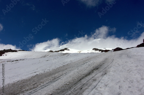 Climbing Elbrus. Snow-capped mountain peaks and figures of climbers in the foreground. Mountains covered with snow. The road to the top of Elbrus.