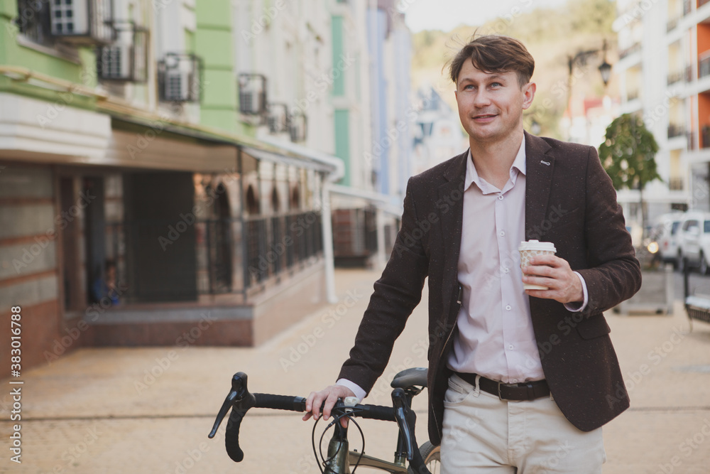 Attractive stylish man enjoying coffee walking in the city with his bike Attractive stylish man enjoying coffee walking in the city with his bike
