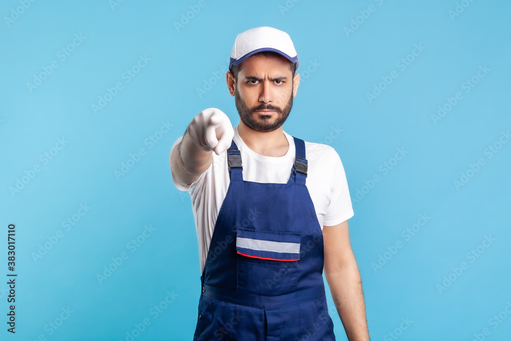 Hey you! Portrait of strict handyman in overalls and cap pointing finger to camera. Profession of service industry, post and delivery, engineer builder job. Expert repairman in workwear making choice