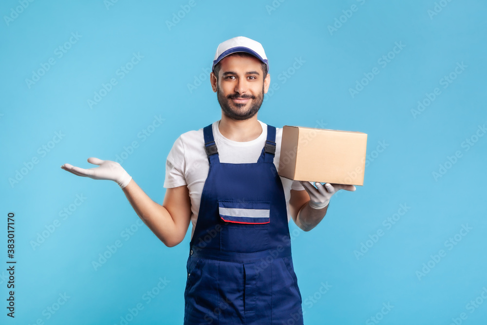 Happy worker in uniform carrying cardboard box and raising other hand to hold empty space, advertising area for commercial image. Concept of cargo transportation, delivery service, express shipping Happy worker in uniform carrying cardboard box and raising other hand to hold empty space, advertising area for commercial image. Concept of cargo transportation, delivery service, express shipping