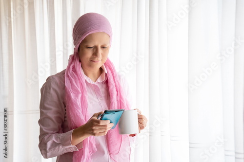 Fototapet Woman with cancer and pink headscarf looking at mobile phone and smiling next to