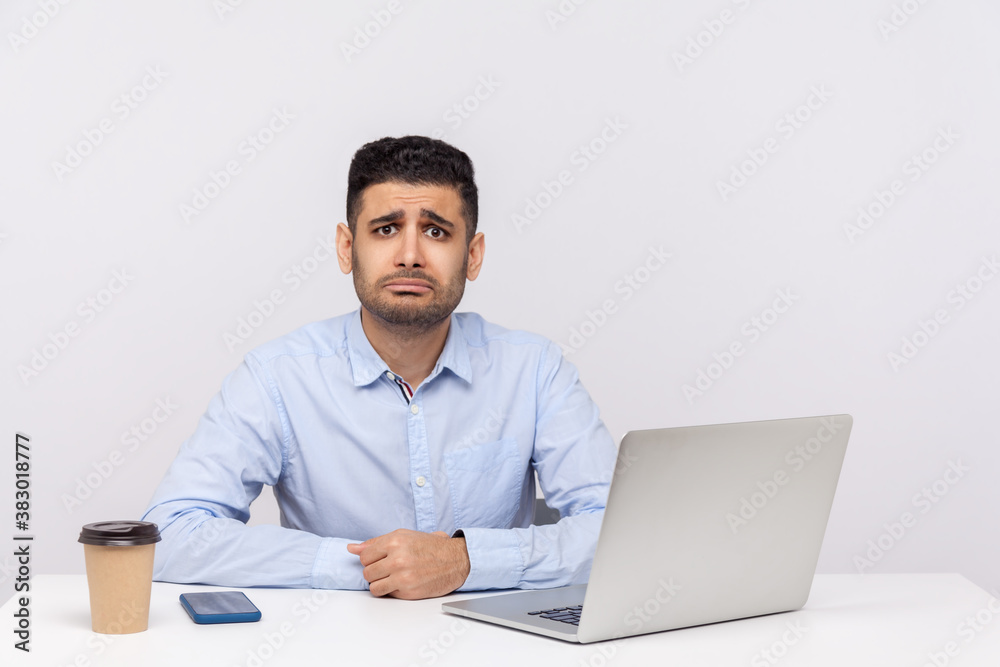 Upset depressed young businessman sitting office workplace, frowning looking at camera unhappy resentful expression, tired bored of stressful job. indoor studio shot isolated on white background Upset depressed young businessman sitting office workplace, frowning looking at camera unhappy resentful expression, tired bored of stressful job. indoor studio shot isolated on white background