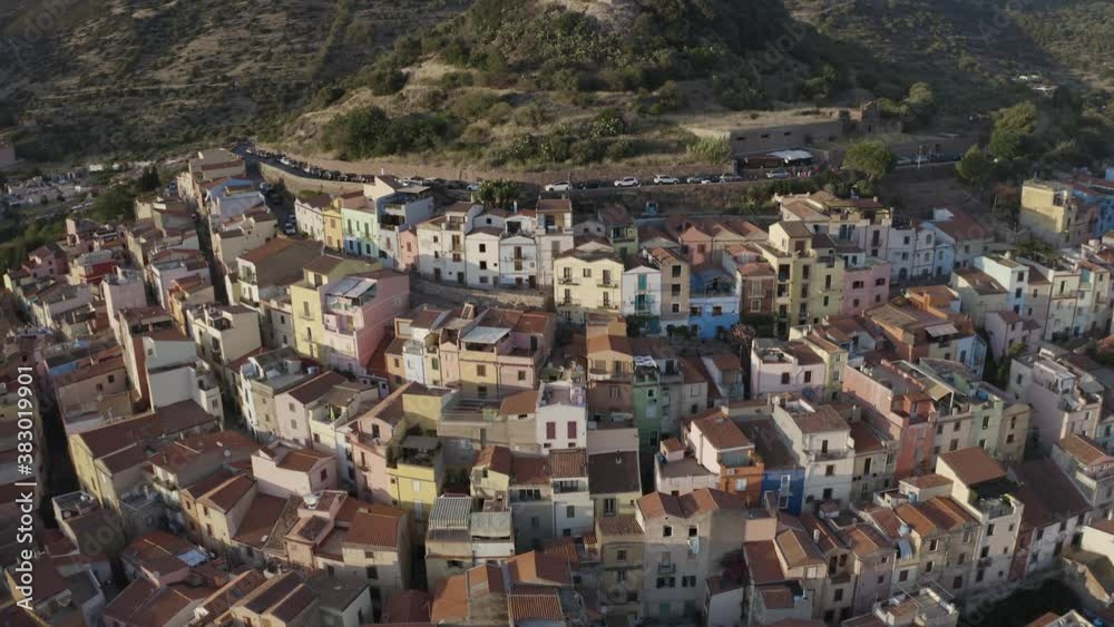 Aerial pan shot city view for buildings surrounded by green mountains and a canal river during sunset. Bosa, Sardinia, Italy and Temo river. Aerial pan shot city view for buildings surrounded by green mountains and a canal river during sunset. Bosa, Sardinia, Italy and Temo river.